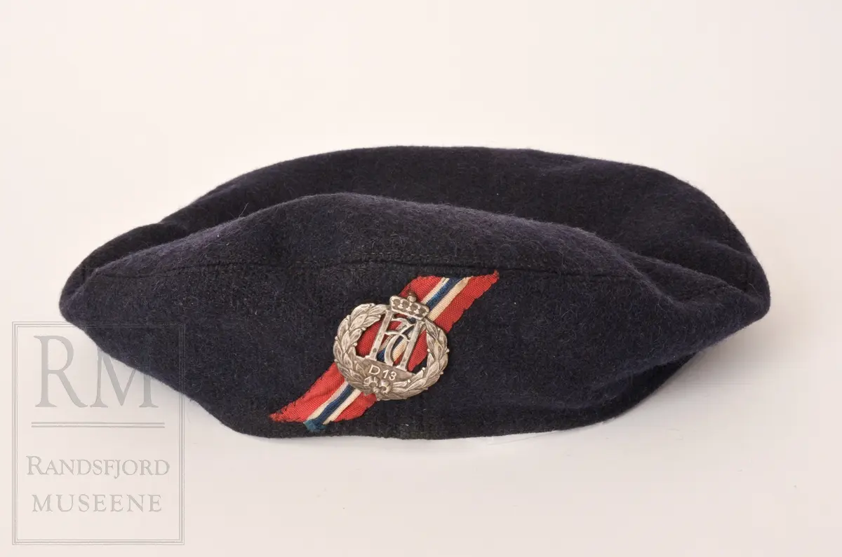 a. Mørk blå kjeledress/ overall med flyvermerke. Militær type. b. Mørk blå lue, berret med H7 luemerke festet og norske farger på bånd. c. Armbind med norske farger. d. Bandolær i lyst brunt lær, messinghemper og spenner. e. Trekantet halstørkle skåret ut av fallskjermstoff (mosegrønn), bit av fallskjermsnor brukt som knyting