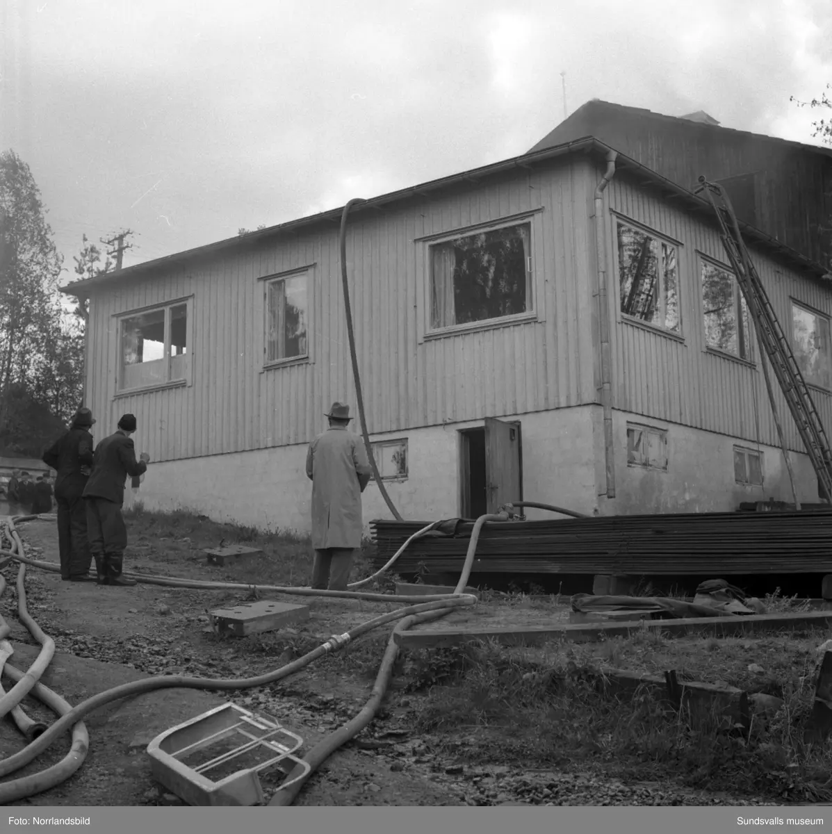 En stor serie bilder från en eldsvåda i kontorsbyggnaden och Bylanders Café vid Luckstaverken, Lucksta ångsåg. Släckningsarbete pågår och massor av människor hjälps åt att rädda så mycket lösöre som möjligt. Elden startade i på övervåningen i kassören Sven Perssons bostadslägenhet. Persson räddade sig ut genom att hoppa från balkongen på baksidan. Brandkårerna från Attmar, Tuna och Sundsvall lyckades till slut få bukt med elden men övervåningen totalskadades och det kafé som fanns inrymt i bottenvåningen fick stora brand- och vattenskador.