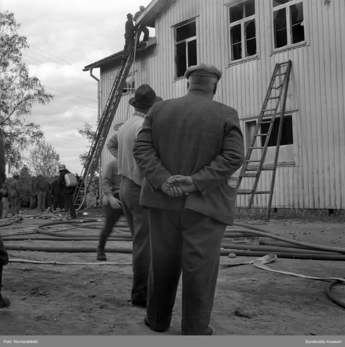 En stor serie bilder från en eldsvåda i kontorsbyggnaden och Bylanders Café vid Luckstaverken, Lucksta ångsåg. Släckningsarbete pågår och massor av människor hjälps åt att rädda så mycket lösöre som möjligt. Elden startade i på övervåningen i kassören Sven Perssons bostadslägenhet. Persson räddade sig ut genom att hoppa från balkongen på baksidan. Brandkårerna från Attmar, Tuna och Sundsvall lyckades till slut få bukt med elden men övervåningen totalskadades och det kafé som fanns inrymt i bottenvåningen fick stora brand- och vattenskador.