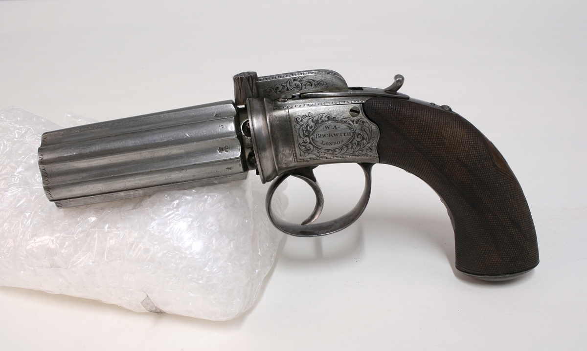 Revolver i "cased set", bestående av revolver (Pepperbox), en enkeltløpet perkusjonspistol samt diverse verktøy, alt liggende i mahognykasse. Bestandelene er følgende: 

KASSE av mahogny, 36,6 x 18,6 x 6,6, cm og er forsynt med lokk som har to mesinghengsler i bakkant. På forsiden er det lås med medding nøkkelhullbeslag på forsiden. Nøkkel av jern, ca. 2,9 cm lang. Midt på lokket er det et rundt messingskilt med profilert kant. Skiltets diameter er 3,8 cm. Kassen er indelt i 11 rom hvorav tre er forsynt med lokk med små, hvite gripehåndtak, runde, knappformede med diameter 1,05 cm. Alle rom er trukket med grønn filt. På lokkets innside er klebet produssentens merkelapp.

REVOLVER. Såkalt "Pepperboks". Et revolverende kammerstykke hvor hver kammer utgjør en selvstendig pipe, en forløper for de senere revolveremed kort tønne og langt løp. Kammerstykket (tønne) er 10 cm langt, hver løp har et kaliber på litt underkant av 10 mm. I bakkant er pipene forsaynt med pistong. På utsiden er pipene ca, 1,2 cm fra pistongene, merket fortløpende med nummer 1 - 6 . Mellom pipene er kammerstykket merket vekselsvis med kronet CP og V. Revolveren har overliggendeslaghane med gravert blomsterranke motiver. Bakenfor hanen er det en bevegelig sikringsfløy. Sideblikkene er prydet med graverte blomsterranker,det venstre sideblikket er markert "W.A. BECHWITH LONDON". Avtrekksbøylen er prydet med blomsterranke motiver. Grepsplater av mørkebrunt tre som er filt i rombemønster. Kolbekappen et oval og svakt buet , er kantet med en smal bord og har i midten et gravert, rundt lokk innenfor hvilket er et lite rom for kuler og fenghetter. Grepet har et lite firkantetntommeskilt med brutte hjørner. Alle beslag er av stål. 

PISTOL. Enkeltløpet, total lengde 13,2 cm. Pipen har et kaliber som revolveren. Pipen er 5,4 cm lang og er stemplet med kronet CP og V. Slaghanene står midt oppå pistolen, stikkende opp mellom sideblikkene. Hanen har skjellmønstret dekor og er forsynt med et par øyne. Når hanen spennes, felles en avtrekker fram under under pistolen. Sideblikkene er dekorert med blomsterranker. Den høyre sideblikket er merket "LONDON" og det venstre "H.BECHWIT ", Grepet er av tre,mørkebrunt og er filt i rombemønster. På grepet sitter et ovalt tommeskilt. 
KRUTTFLASKE. Av messing, 11,4 cm lang, flaskeformet, noe flattrykt mot den nedre delen hvor  det vider seg ut i bredden. Festeskrue og fjær for lukkemekanisme er av stål. 
LADE7PUSSESTOKK. av gulfarget med  et 4,6 cm riflet mesinghode. Total lengde 17,6 cm. Vekt.: 14g. 
KULETANG. Av jern, 8,6 cm lang, merket "1". Vekt: 45 g. 
KULETANF. Av jern, 11,5 cm lang, merket "82". Vekt: 44 g. 
PISTOLNØKKEL. For fjerning og innsetting av pistonger på revolveren. 11,3 cm langt og med sortlakkert treskaft. Vekt. 17 g.