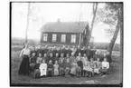 Rinkaby skola, 39 skolbarn och lärarinna fröken Hanna Gustafsson.
Skolbyggnad i bakgrunden.