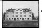 Hörnhuset vid Oskarstorget, trevånings hyreshus med frontespisar, två tornhuvar, brutet plåttak.