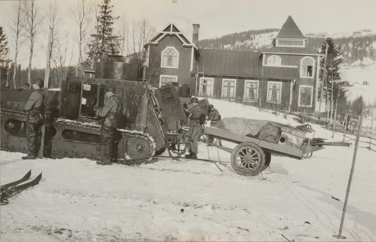 Soldater bredvid stridsvagn m/1921 (eller m/1921-1929) framför ett trähus. Stridsvagnen har ett släp försett med skidor bakom sig.