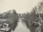 En kanal med björkar, roddbåtar och hus längs stränderna.