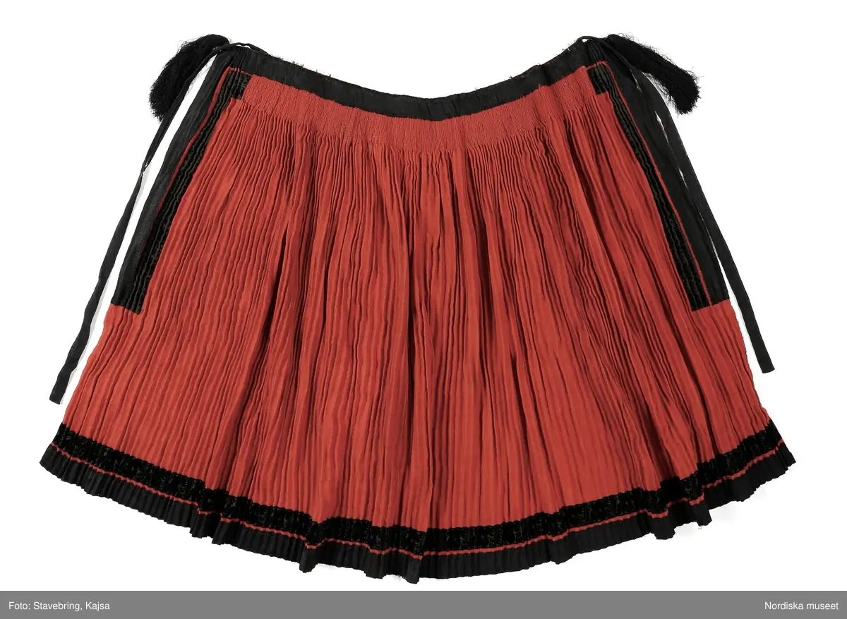 Huvudliggaren:
"Hollands draegt fr. Köpenhamn
Bestående af:
a) Kafetröje med Spaender [tillägg i blyerts.] skall vara kravetröje - 30 kr [spännet ommärkt till e+ 2011-03-08]
Spännet märkt: M.H.P.D.
b) Skjört - 28 kr
c) Forklaede med spaender - 30 kr
d) Haette med tillbehör och Haandstycke - 6 kr
e+) [spännet ommärkt till e+ 2011-03-08] Spännet märkt: M.H.P.D.
Ink. ss 20.087 [=ink. hos fru m. Wildschiödz i Köph. ss 20.001 [= gm (genom) dr A. Hazelius i Stockholm.]]- 94 kr. Under hösten 1877."
