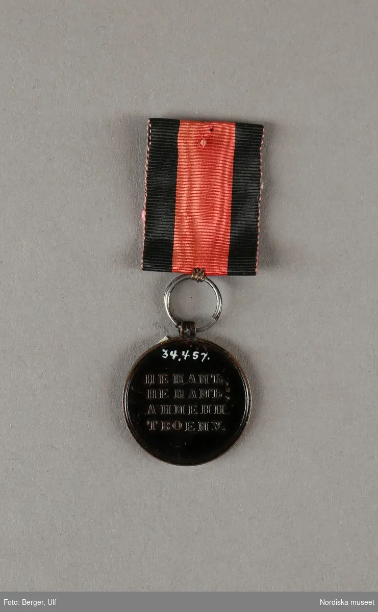 Huvudliggaren:
"Medalj. Se 34.443 [= 34.443-34.485 samlade af friherre Bennet.] 
I tenn, svartmålad. Å ena sidan: Det allseende ögat med strålar; nederst 1812 [och 4 "bokstäver]. Å andra sidan 'HE HAMb, HE MAb ANMEHN TBOEMY [liknande, trol. kyrilliska bokstäver, se huvudliggaren för korrekt avskrift], i fyra rader. Diam. 8 1/2 lin. I rödt, vattradt sidenband med svarta kanter.
Ink. ss. 34.424 [=ink. ss. 34.422  jämte 34.425-34.485]. [34.422=Ink. af byggmästare E. A. Boman i Stockholm 8/1 1883]"