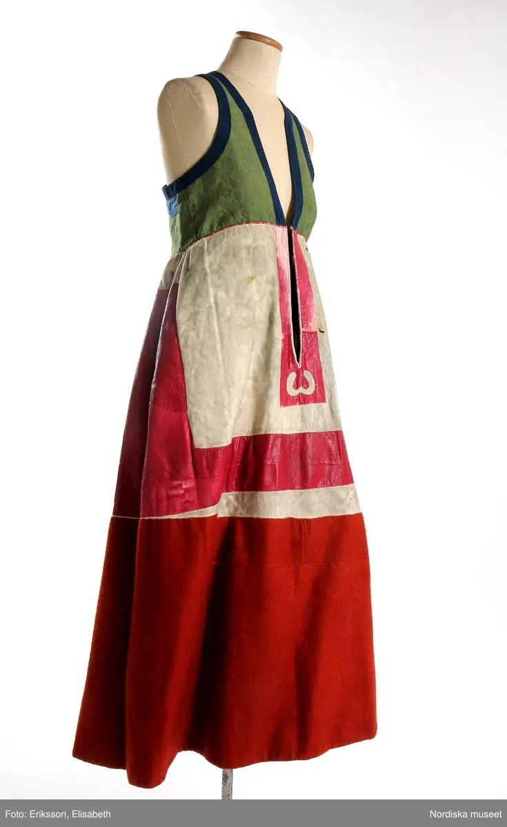 Livkjol, s.k. päls eller skinnklocka. Röd kjol,  där övre halvan består av rött saffianskinn med 7 centimeter bred vit kant överst, och ett vitt fält mitt fram,  nedre halvan av röd vadmal, 3 våder  hela kjolen fodrad med fårskinnspäls och nedtill oblekt linnelärft och är mycket tung. Täta stripade rynkor runtom i midjan utom ett slätt parti 15 cm på var sida om mittsprundet fram. Nedanför sprundet mönster i applikation med vittt skinn på rött . Livstycket är av mönstervävt grönt kamgarnsylle med flotterande blommönster på tuskaftsbotten. 2 framstycken, 1 ryggstycke, kantat med indigo blå 2,5 cm breda bomullsband kring ärmhål hals, framkanter, i vinklar på ryggen blå sidenband.  Livet fodrat med  linnelärft.  En hake och hyska i mässing i midjan, för övrigt ingen knäppning. Har sannolikt snörts fram genom maljor, troligen med en silverkedja.
Det gröna mönstrade tyget var vanligt runt 1800, troligen en importvara från England. Fanns i olika färger.
Se Österlens Folkdräkter, 1999:  Christina Lindwall-Nordin:  Bredhöftade matronor i tjocka kjolar, sid 56-59.
/Berit Eldvik 2012-08-14