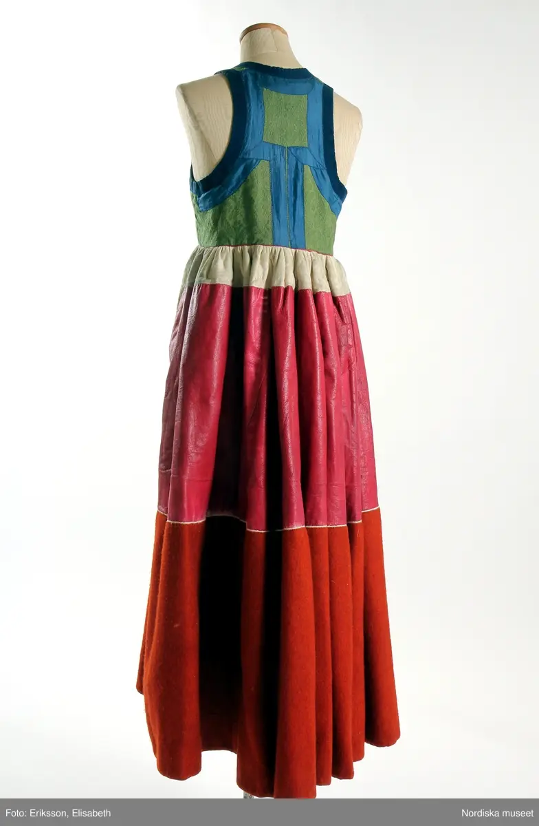 Livkjol, s.k. päls eller skinnklocka. Röd kjol,  där övre halvan består av rött saffianskinn med 7 centimeter bred vit kant överst, och ett vitt fält mitt fram,  nedre halvan av röd vadmal, 3 våder  hela kjolen fodrad med fårskinnspäls och nedtill oblekt linnelärft och är mycket tung. Täta stripade rynkor runtom i midjan utom ett slätt parti 15 cm på var sida om mittsprundet fram. Nedanför sprundet mönster i applikation med vittt skinn på rött . Livstycket är av mönstervävt grönt kamgarnsylle med flotterande blommönster på tuskaftsbotten. 2 framstycken, 1 ryggstycke, kantat med indigo blå 2,5 cm breda bomullsband kring ärmhål hals, framkanter, i vinklar på ryggen blå sidenband.  Livet fodrat med  linnelärft.  En hake och hyska i mässing i midjan, för övrigt ingen knäppning. Har sannolikt snörts fram genom maljor, troligen med en silverkedja.
Det gröna mönstrade tyget var vanligt runt 1800, troligen en importvara från England. Fanns i olika färger.
Se Österlens Folkdräkter, 1999:  Christina Lindwall-Nordin:  Bredhöftade matronor i tjocka kjolar, sid 56-59.
/Berit Eldvik 2012-08-14