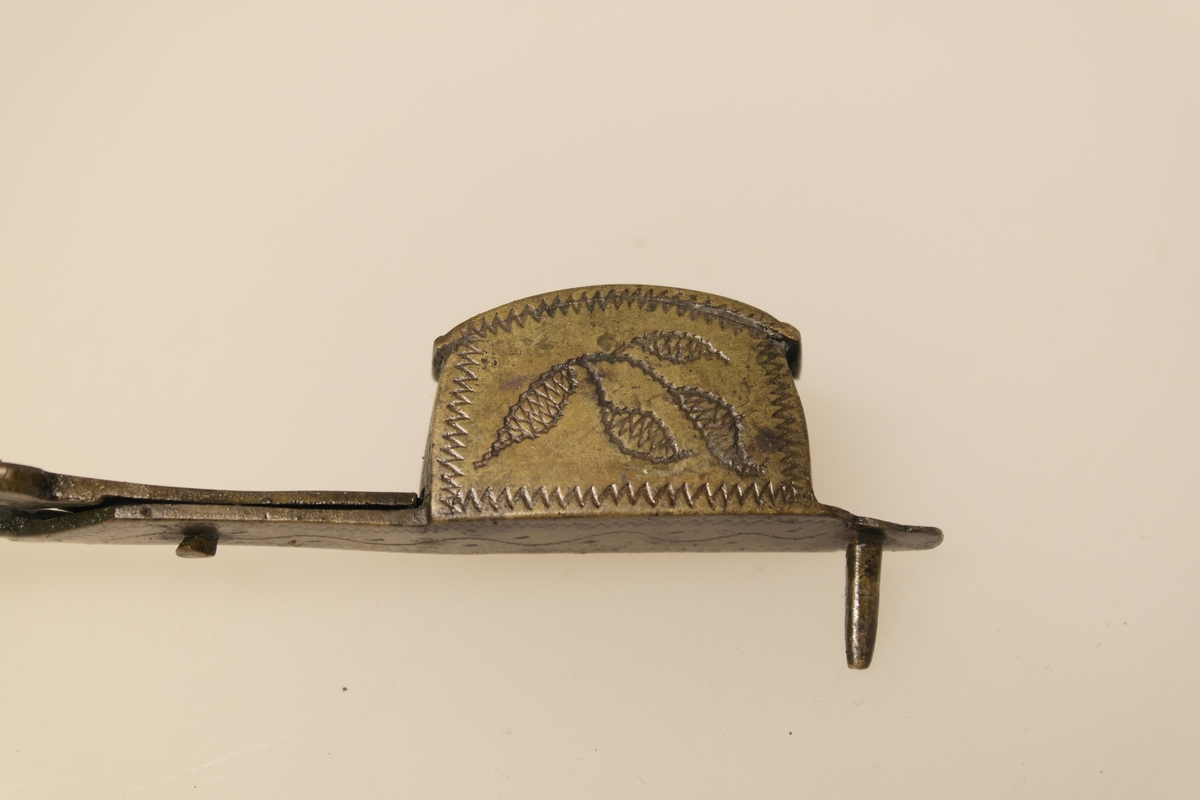 Lyssaks i støpt, pusset og siselert messing. Inngravert ornamentikk: sikksakk og bølgeborder.
