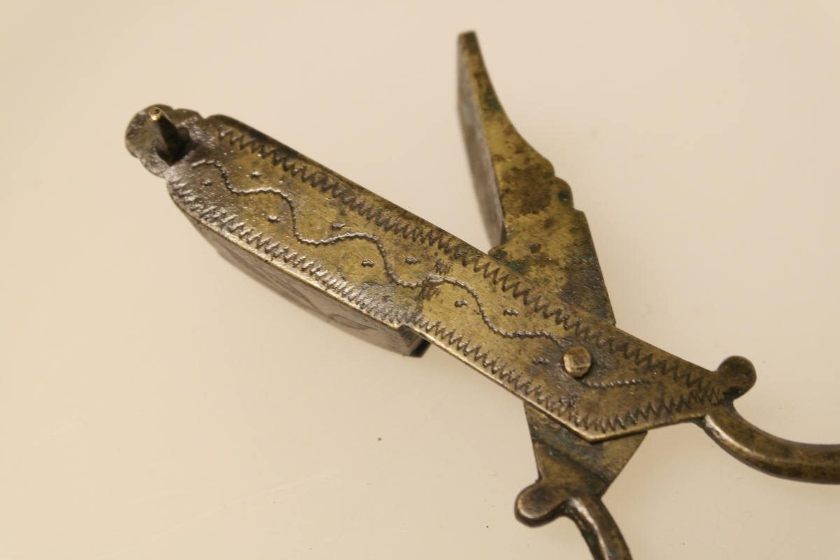 Lyssaks i støpt, pusset og siselert messing. Inngravert ornamentikk: sikksakk og bølgeborder.