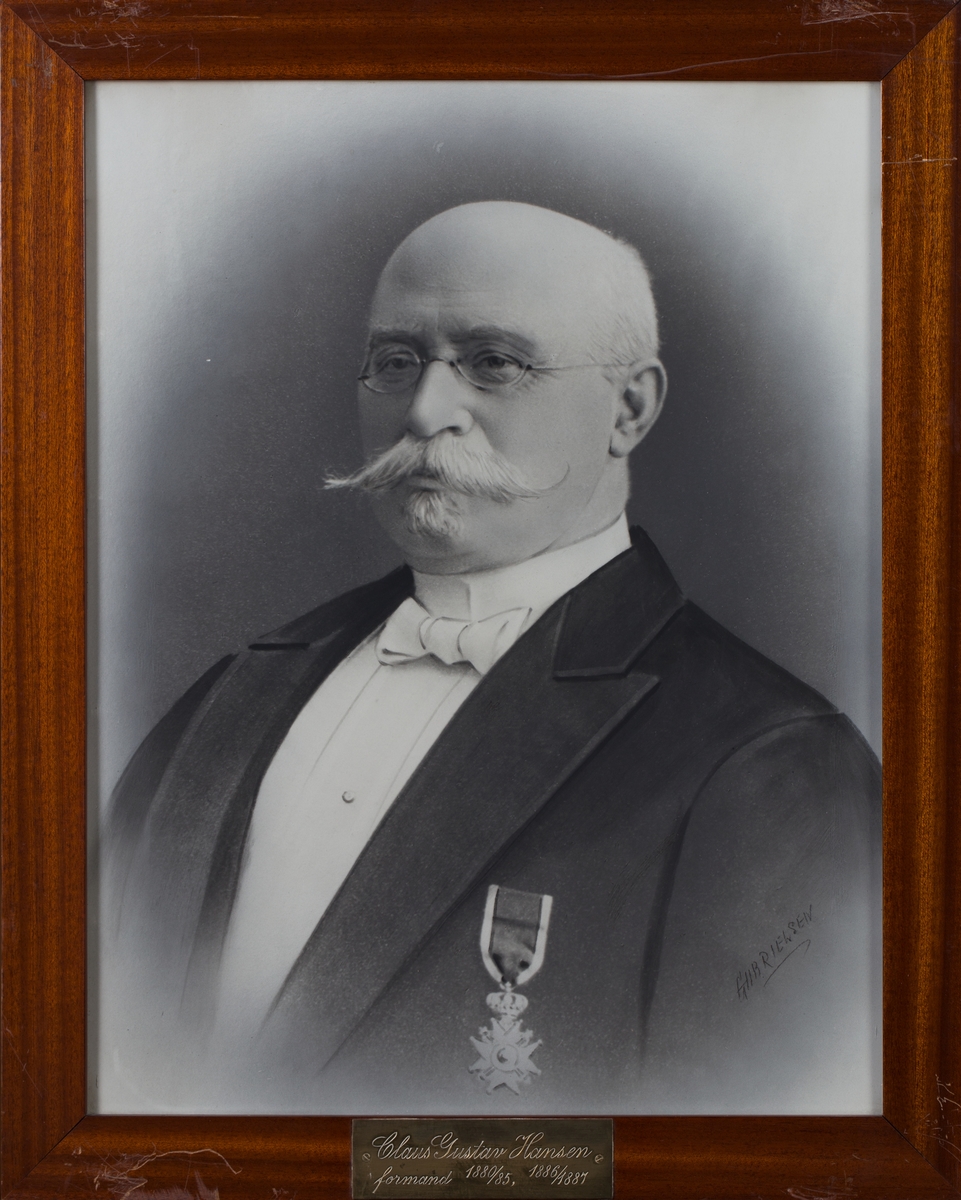 Portrett av apoteker Claus Gustav Hansen med briller. Mørk dress, orden/medalje på frakkebryst. Brystbilde.