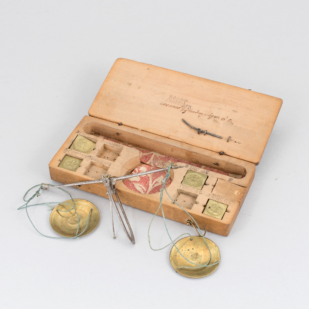 Myntvåg med etui. Vågbalk av järn med spatelformade ändar och åttaformade fästen. Visare av järn med fäste format som ett ankare. Kupiga vågskålar av mässing med inslaget mästarmärke, CM 8 i cirkel. I var skål tre hål för upphängning. Etui av valnötsträ med åtta fack för vikter var av ett med skjutlock.  Fyra kvadratiska stämplade vikter med myntbild för, Doublon, Carolin och Ducat samt mindre punsade balansvikter i skala 4 - 5. I övre delen av etuiet utskuret urtag för balansvåg. I etuiets lock en stålpinne för att lyfta vikterna ur sina fack. I lock stämpel med text Recht abgesogen (= riktigt avpassat) och annan otydd text på tyska. 10 delar totalt.