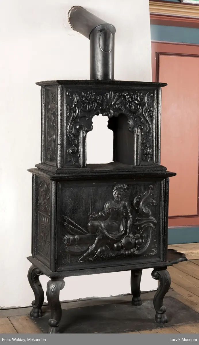 Ovn i  2 etasjer. 
Rokokko, jfr. nr 411 i Norsk Jernskulptur b II 
1. etasje langside: Mars sitter på en kanon med sverd i høyre hånd. Riflet bunn.
1 etasje kortside: Øverst: Rokokko-ornament, nederst: Grevekrone monogram. FL og 1756 
nederst: ovnsdør 2 hengsler ovalt askebrett med profilert kant.
2.etasje langside: Fyldig rokokko-ornament. med blomster. Uregelemessig portalåpning. 
2. etasje kortside: Rokokko-ornament, 
Ovnen har sungne ben m/dyreføtter