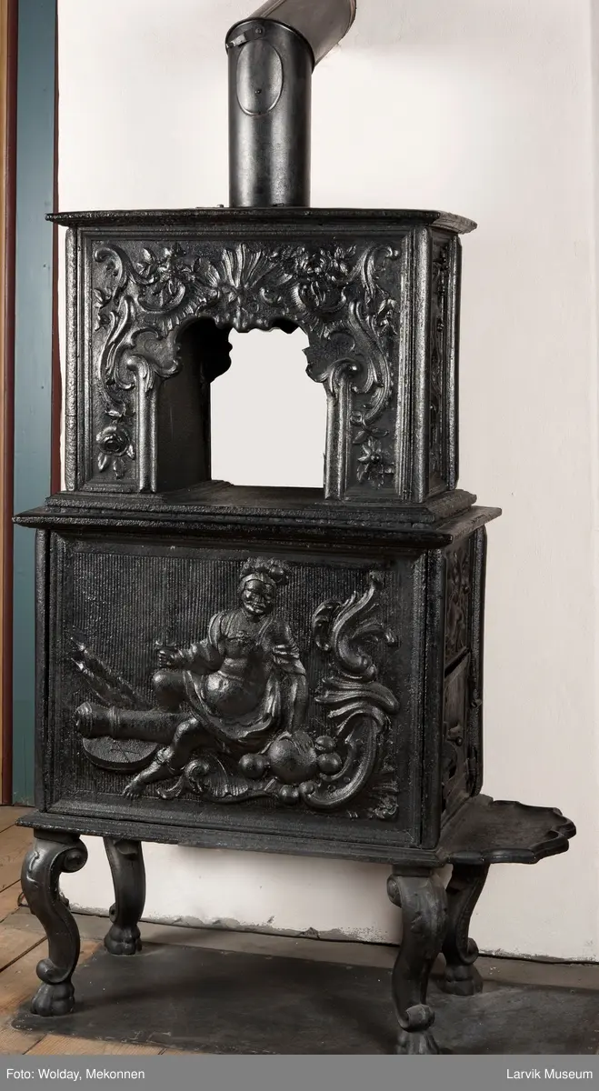 Ovn i  2 etasjer. 
Rokokko, jfr. nr 411 i Norsk Jernskulptur b II 
1. etasje langside: Mars sitter på en kanon med sverd i høyre hånd. Riflet bunn.
1 etasje kortside: Øverst: Rokokko-ornament, nederst: Grevekrone monogram. FL og 1756 
nederst: ovnsdør 2 hengsler ovalt askebrett med profilert kant.
2.etasje langside: Fyldig rokokko-ornament. med blomster. Uregelemessig portalåpning. 
2. etasje kortside: Rokokko-ornament, 
Ovnen har sungne ben m/dyreføtter