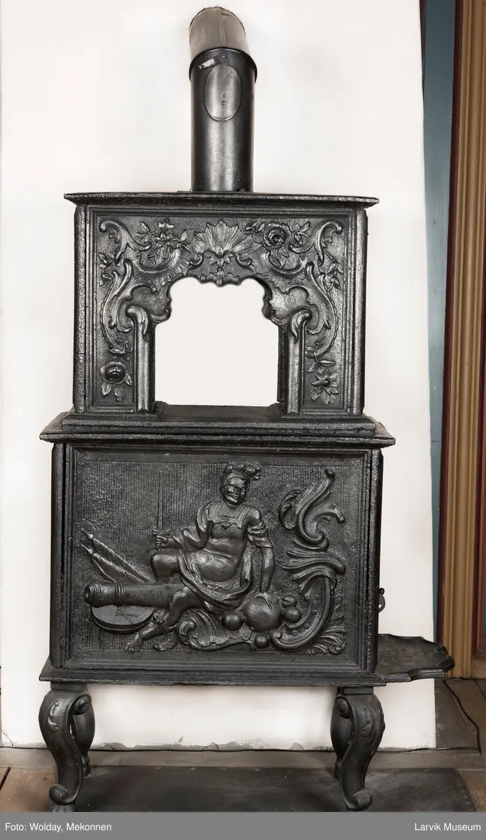 Ovn i  2 etasjer. 
Rokokko, jfr. nr 411 i Norsk Jernskulptur b II 
1. etasje langside: Mars sitter på en kanon med sverd i høyre hånd. Riflet bunn.
1 etasje kortside: Øverst: Rokokko-ornament, nederst: Grevekrone monogram. FL og 1756 
nederst: ovnsdør 2 hengsler ovalt askebrett med profilert kant.
2.etasje langside: Fyldig rokokko-ornament. med blomster. Uregelemessig portalåpning. 
2. etasje kortside: Rokokko-ornament, 
Ovnen har sungne ben m/dyreføtter