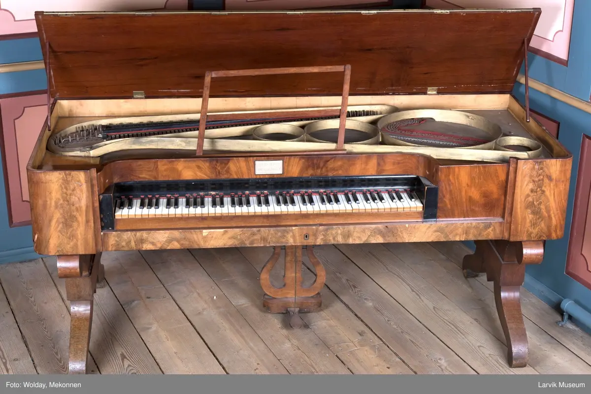 Rektangulært, stekt svugne ben tilnærmet. c-form korte bindn. under lokkplate med glass hvor signert Jens Hoff, Laurvig en pedal festet til pedalfot(?)