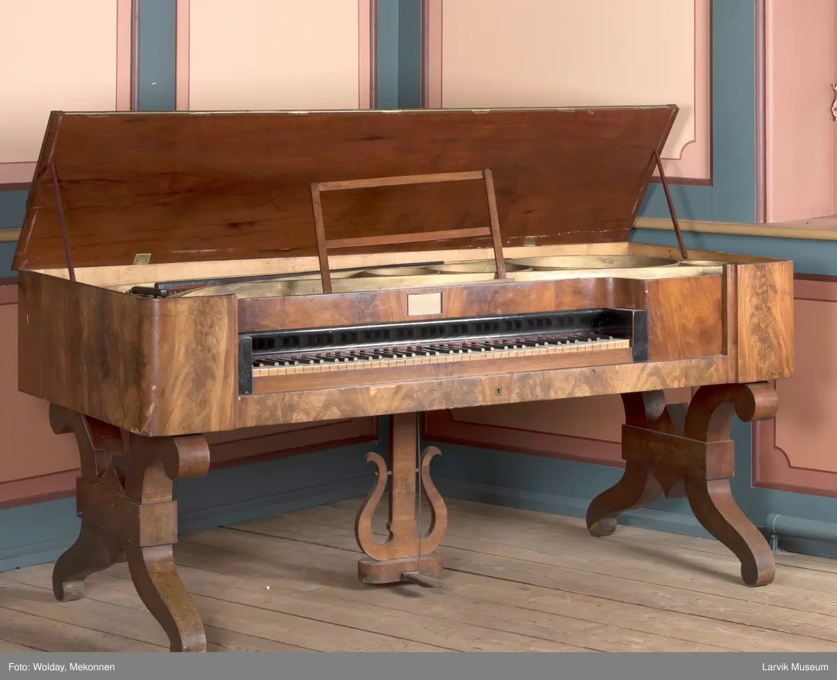 Rektangulært, stekt svugne ben tilnærmet. c-form korte bindn. under lokkplate med glass hvor signert Jens Hoff, Laurvig en pedal festet til pedalfot(?)