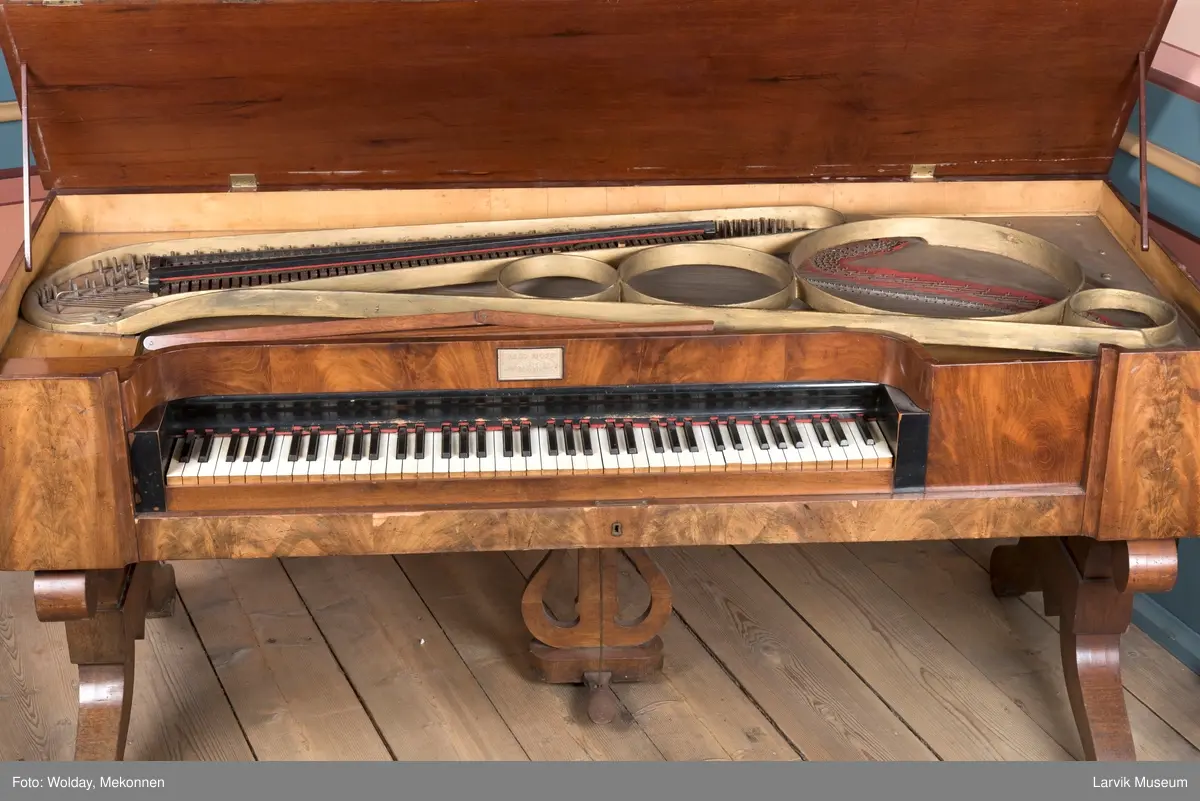 Rektangulært, stekt svugne ben tilnærmet. c-form korte bindn. under lokkplate med glass hvor signert Jens Hoff, Laurvig en pedal festet til pedalfot(?)