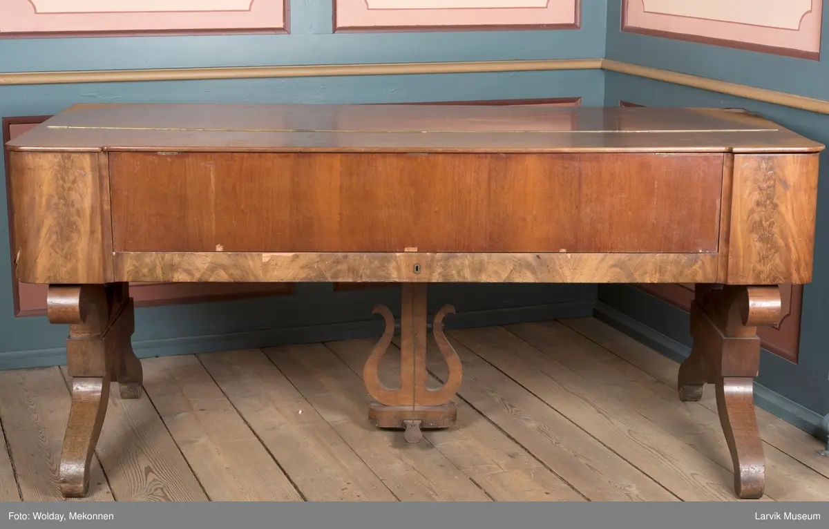 Rektangulært, stekt svugne ben tilnærmet. c-form korte bindn. under lokkplate med glass hvor signert Jens Hoff, Laurvig en pedal festet til pedalfot(?)