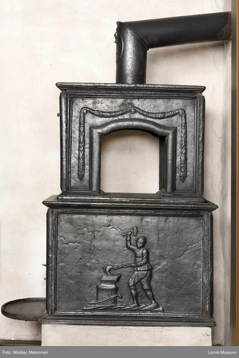 Jernovn med to etasjer, begge er rektangulære. Ovn står på muret fot/understell.
1etasje langside: Vulkan som smed .
1etasje kortside: Musling. 
2etasje langside: Buet åpning i profilert innramming omgitt av girlander. 
2etasje kortside: Overflødighetshorn.