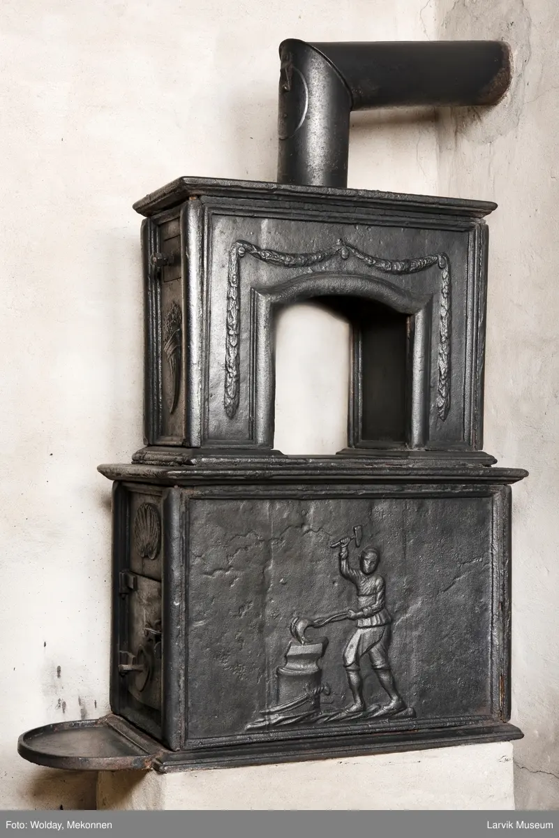 Jernovn med to etasjer, begge er rektangulære. Ovn står på muret fot/understell.
1etasje langside: Vulkan som smed .
1etasje kortside: Musling. 
2etasje langside: Buet åpning i profilert innramming omgitt av girlander. 
2etasje kortside: Overflødighetshorn.