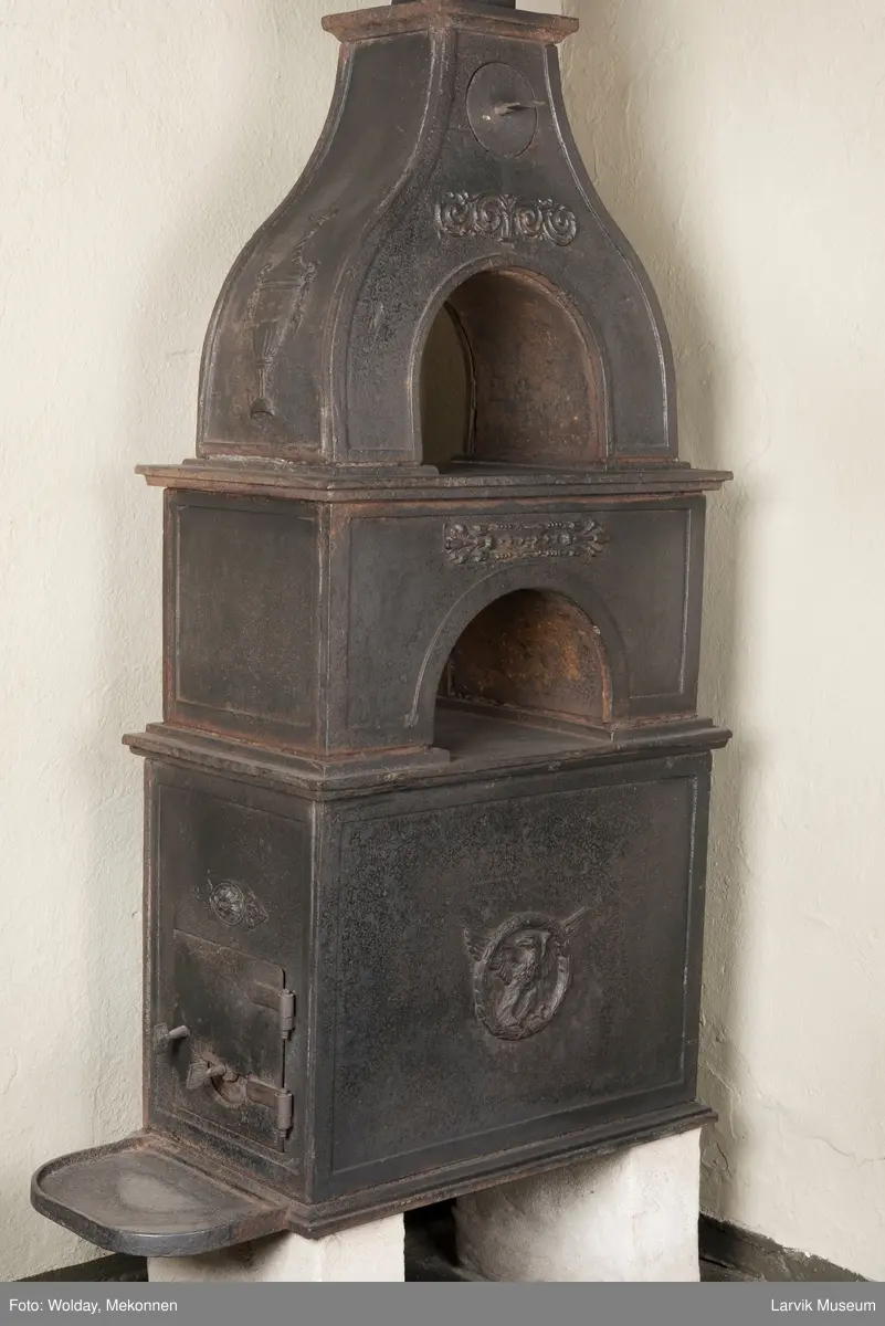 Jernovn i tre etasjer med muret fundament. Langs topp og rundbuet åpning rankeornament. Flatt askebrett med buede hjørner. 
1. etasje langside: Ørn i laurbærkrans 
1. etasje kortside: mrk.: FRITZØE