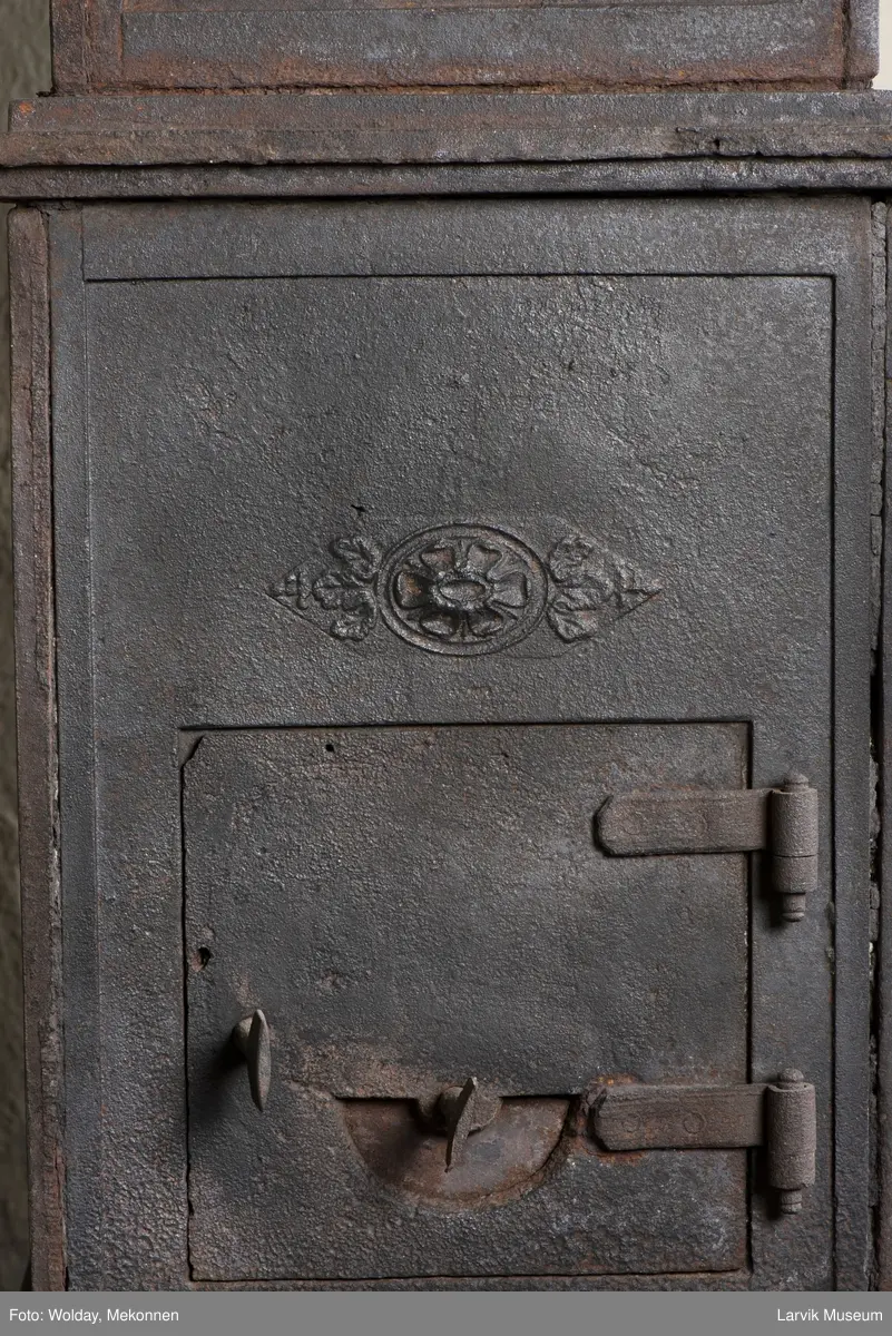 Jernovn i tre etasjer med muret fundament. Langs topp og rundbuet åpning rankeornament. Flatt askebrett med buede hjørner. 
1. etasje langside: Ørn i laurbærkrans 
1. etasje kortside: mrk.: FRITZØE