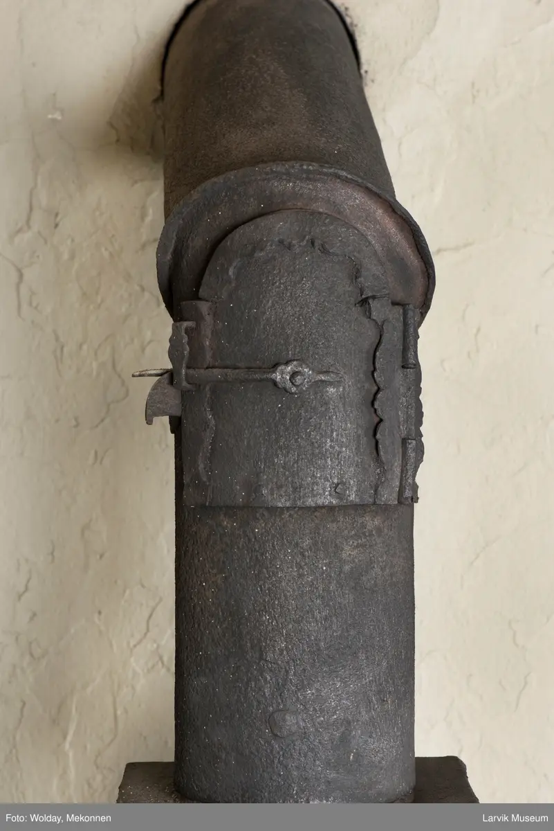 Jernovn i tre etasjer med muret fundament. Langs topp og rundbuet åpning rankeornament. Flatt askebrett med buede hjørner. 
1. etasje langside: Ørn i laurbærkrans 
1. etasje kortside: mrk.: FRITZØE