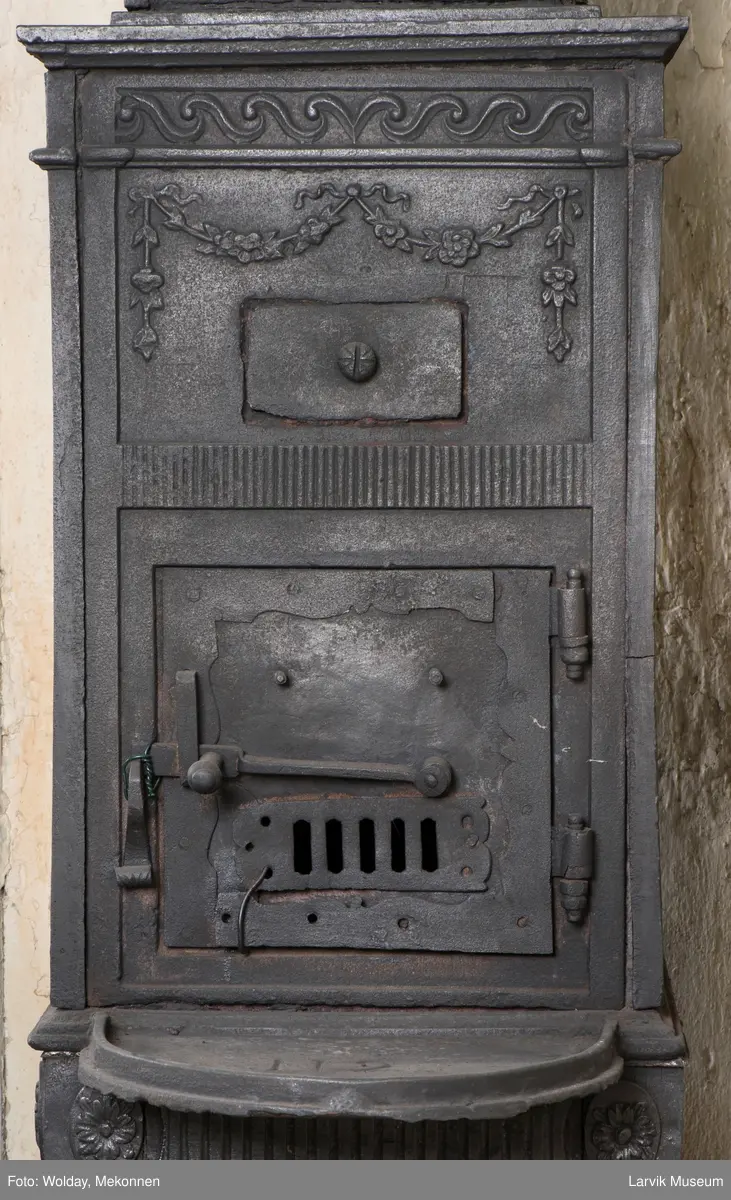 Tredelt , nederste etasje rektangulær fyrkasse/midtf.portalf/pyr.t. ben og sarg med kannelyrer og rosett i tre.  1.etasje langside: bladmedaljong, kvinne ved alter, øverst bølgemeander. 1.etasje kortside: bølgemeander, girlander og rosett 2.etasje langside: rundbuet åpning, i de øvre hjørner 2. etasje kortside: rosett i rektangel topp langside: palmett og rosett topp.Kortside: rosett i rektangel