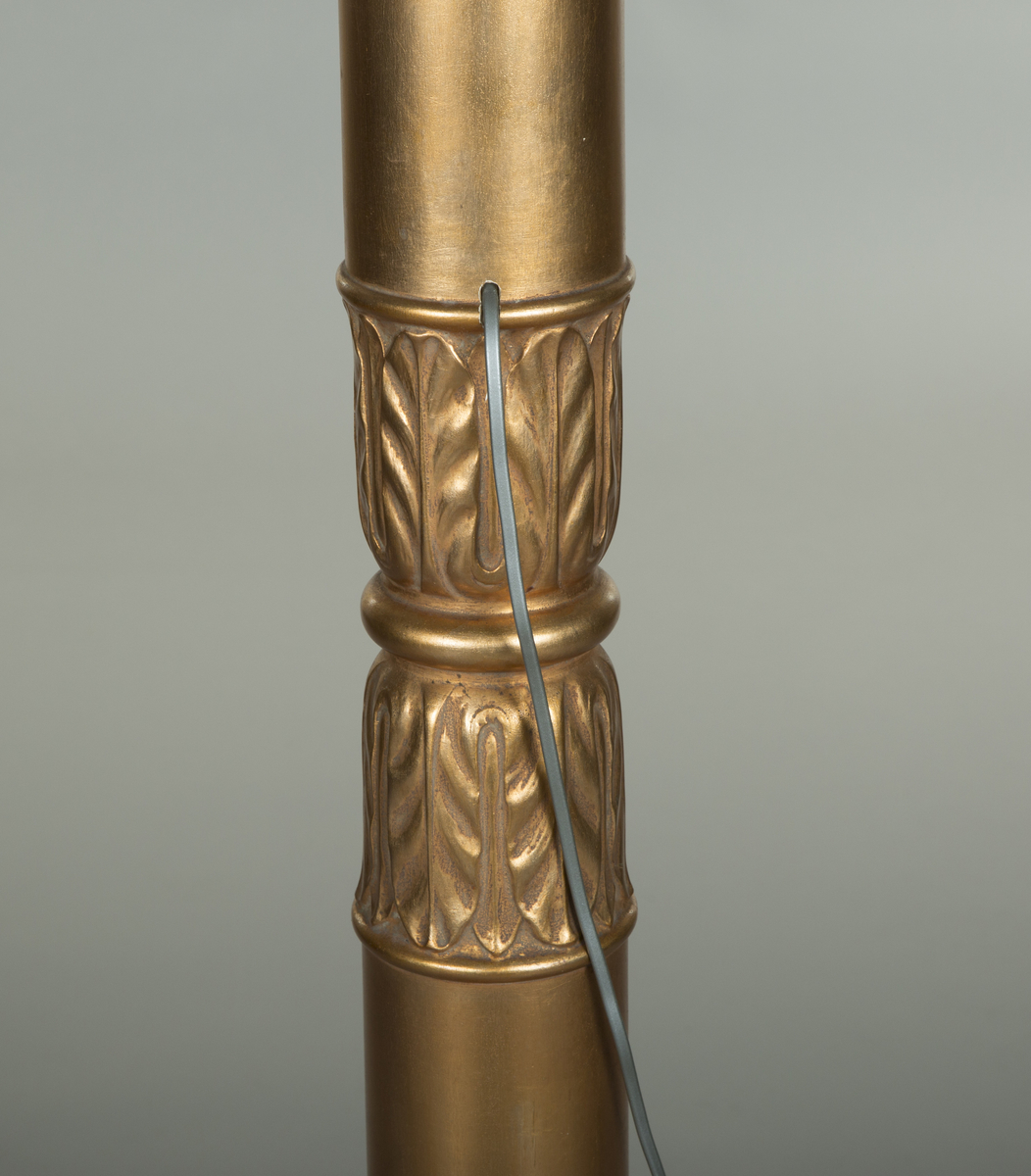 Forgylte gulvstående lamper for flere lys, både stearinlys og elektrisk. Hull til stearinlys langs kanten på hele topp-platen. En åpen lampeskjerm i glass omkranser det elektriske lyset midt på abakus, med bølgende kant (som en fakkel). Lampen er formet som en frittstående gresk søyle med base. Glatt utforming, med et område med bladutskjæringer like under midten, samt på kapitélet. Rund abakus og firkantet base.