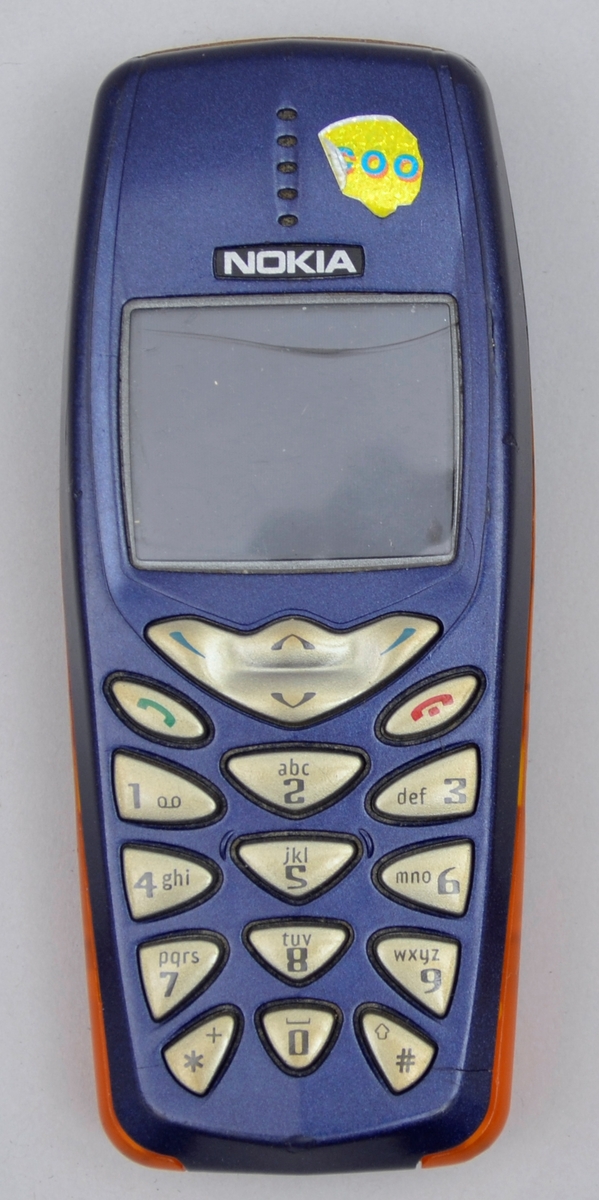 Rektangulær. Tastar og liten skjerm på eine sida. Blå med detaljar i oransj på sidane. Batteri.