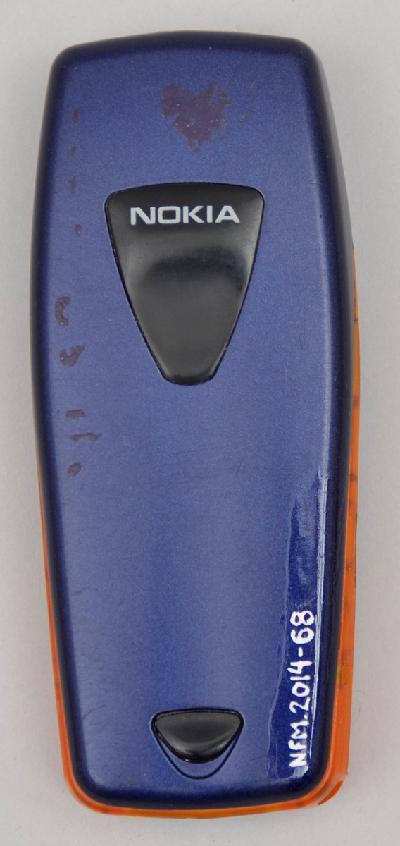 Rektangulær. Tastar og liten skjerm på eine sida. Blå med detaljar i oransj på sidane. Batteri.
