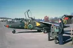 Flygplan SK 60 märkt nummer 70 ur F 5 Krigsflygskolan står på flygfältet på Malmen, 1973. Bredvid står en tekniker vid en startvagn.