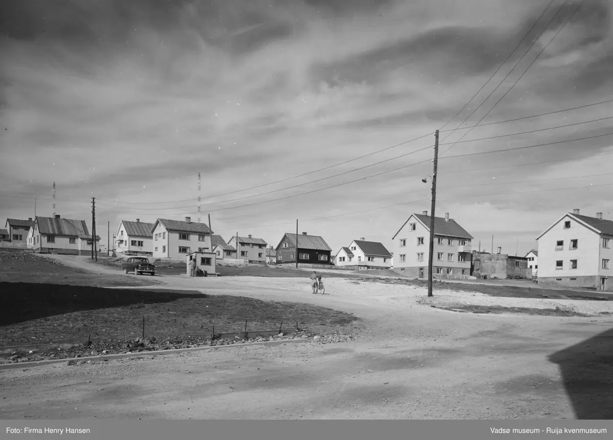 Vadsø sentrum på 1950-tallet. Bildet er tatt fra krysset Oscarsgata - Tollbugata og viser bygninger langs østsiden av Tollbugata opp mot Damsveien. Vi ser NRKs to radiomaster, og hus som ligger langs Damsveien.