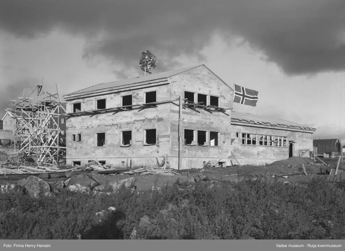 Vårbrudd 1949.  Bildet viser Vårbrudd under oppføring. Bygningen har nå "tett tak" og vi ser kransen som er heist på mønet og flagget vaier. Forskalinger og bygningsmaterialer ses rundt bygningen. I høyre billedkant skimtes en nissenbrakke.