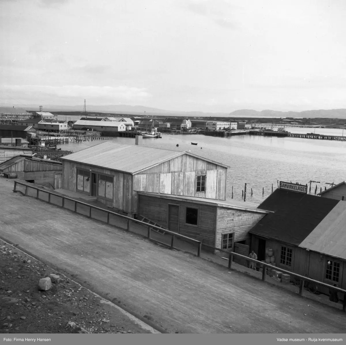 Havnegata 1951. I bakgrunnen litt av havna og østre del av Vadsøya med luftskipsmasta. skilt med "Samvirkelaget" på et tak: Dampskipskaia, antagelig under bygging, flere nybygg , reisverk for nye bygg, og rester av krigsskadde kaier.