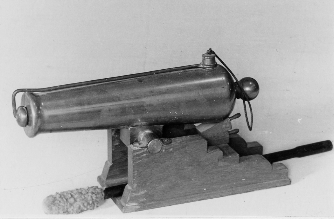 Modell av kanon (Signalkanon). 23 mm slättborrad framladdningskanon
Försedd med trumf och kulformad druva. Inga sirater. Löv på kanonens undersida med tappar av stål. Lavett av polerad ek, senare utförd som museimontage, bestående av två baktill trappstegsformade lavettsidor samt ett bottenplan. Överfall av mässing. 2 st riktkilar av polerad ek, hoplimmade inbördes och med lavetten.
Tillhörande mynningspropp fästad till metallstång i vars andra ända är anordnat skyddslock för fänghålet. Stången är försäkrad till druvan med en stjärt av tjärat tågvirke.
I B 97
Viskare och sättare på en gemensam stång av svartmålad trä.
Har tillhört 'Sköldmön”.