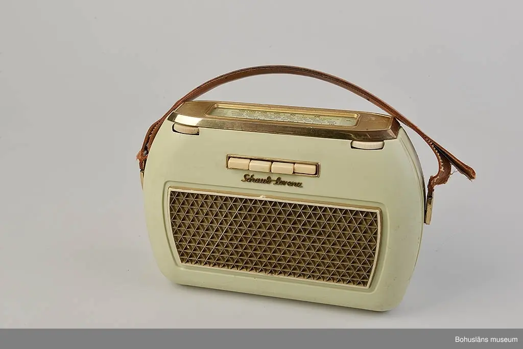 Ljusgrön transistorradio av fabrikat Schaub-Lorentz, Pforzheim, Tyskland.
Fyra vita knappar och högtalare fram. Vridbara programväljare på ovansidan med olika våglängder utmärkta. Två hjul att ställa  in program med. Kortsidorna har rundad form. Bärhandtag av brunt läder. På baksidan står det: "TRANSISTO...".
Batteri, 4 st 1.5 volt, modell RZ0.