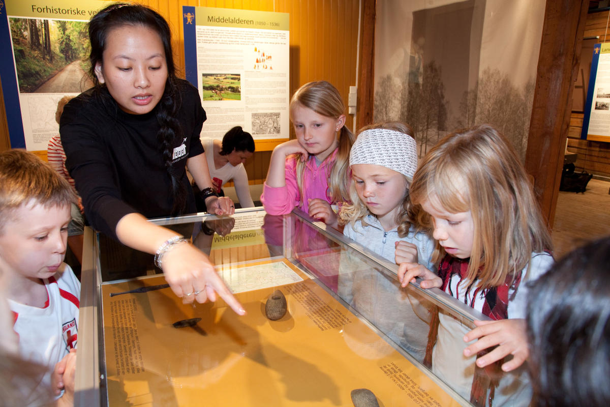 Omviser viser elever fra 3. trinn forhistoriske gjenstander som ligger i et monter.