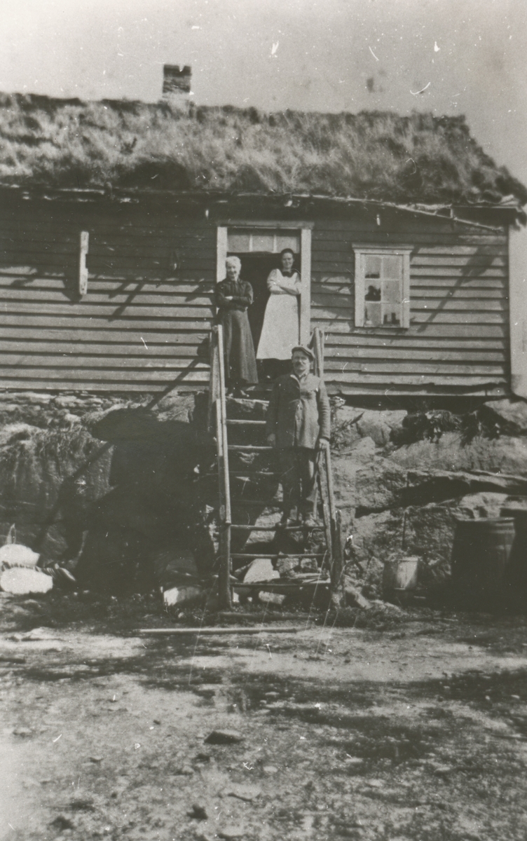 En mann og to kvinner på en trapp foran et hus.