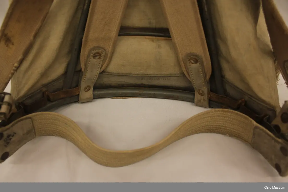 Ryggsekk til turbruk; seilduk/canvas, lærbesetning, metallmeis. Fóret lokk i bomull, lerretsbinding. Kraftige stropper i canvasbånd. Krysstropper i rygg i kanvasbånd. To sidelommer og en stor forlomme. Glidelåslomme på innsiden av lokk.