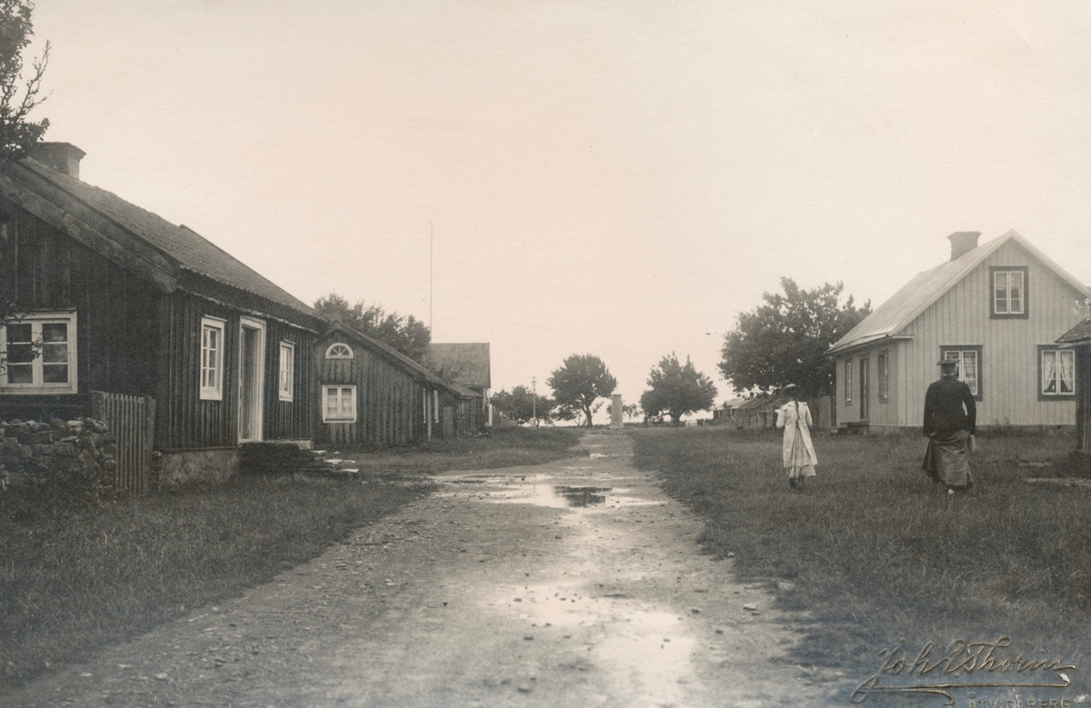 Gata i Mörbylånga kring sekelskiftet 1900. Vy söderut vid korsningen Västerlånggatan-Hantverksgatan mot pump ovan brunn grävd 1892, i det som idag är korsningen Västerlånggatan-Esplanaden. Esplanaden var ej anlagd vid tiden för fotot. Idag syns bortom pumpen Köpingsskolan uppförd 1913.