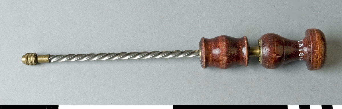 Drillborr med svarvade handtag av trä. Drillborren består av en 195 mm lång spiralstång med diameter 6 mm. På denna sitter ett svarvat handtag, som när det föres nedåt får stången att snurra medsols och det motsatta hållet när det föres tillbaka. Längst ner på stången sitter ett borrfäste i mässing där en borr med mycket liten diameter fästes. Vid borrning föres handtaget nedåt. Tryck och riktning av borren görs med det svarvade handtaget som stången i den övre delen roterar runt i. Handtagen är rödbetsade och har mässingsbeslag. Det övre beslaget är märkt D.R.G.M.

Funktion: Manuellt driven hållare för borrstål, kan köras både med- och motsols