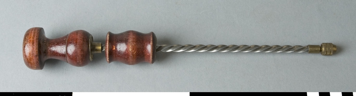 Drillborr med svarvade handtag av trä. Drillborren består av en 195 mm lång spiralstång med diameter 6 mm. På denna sitter ett svarvat handtag, som när det föres nedåt får stången att snurra medsols och det motsatta hållet när det föres tillbaka. Längst ner på stången sitter ett borrfäste i mässing där en borr med mycket liten diameter fästes. Vid borrning föres handtaget nedåt. Tryck och riktning av borren görs med det svarvade handtaget som stången i den övre delen roterar runt i. Handtagen är rödbetsade och har mässingsbeslag. Det övre beslaget är märkt D.R.G.M.

Funktion: Manuellt driven hållare för borrstål, kan köras både med- och motsols