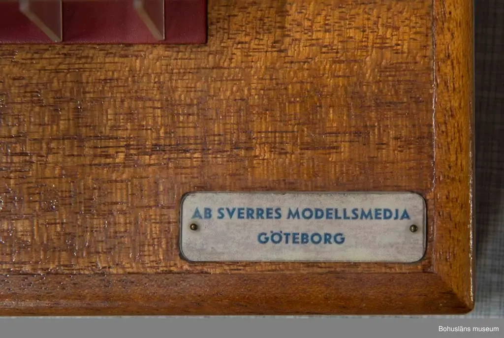 Modell av sektion till bulklastbåt stående på en träsockel.
Färgen är röd och grön + genomskinlig plast.
Märkningar på båda sidor på sockeln: "AB Sverres modellsmedja Göteborg".
