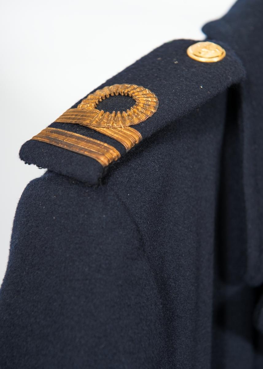 Dubbelknäppt långkavaj med 4 knappar. Vertikala ficköppningar utan lock. Axelklaffar med löjtnants gradbeteckning.