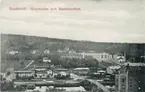 Vy över Norrmalm. Gamla gångbron (kallad Puckelbron och Kamelryggen) över Selångersån. Bron raserades vid vårfloden 1919. Lasarettet och stadsbacken. Hydéns möbelaffär ses till vänster efter Skepparegatan. Ett av varumagasinen i nedre höger kant. Vykort.