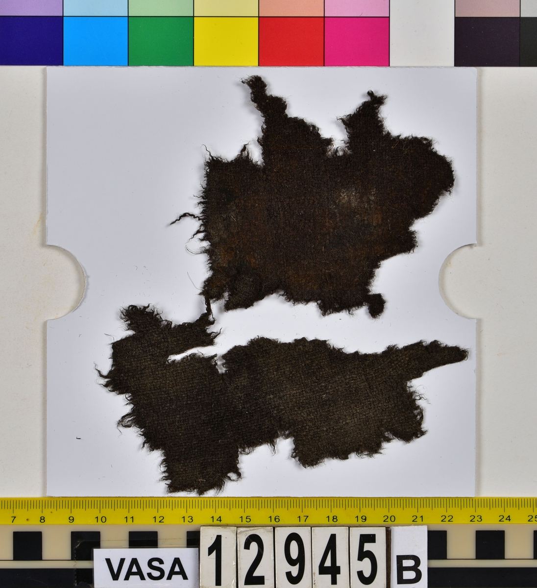 Textilfragment.
15 textilfragment uppdelade på fyndnummer 12945a-g.
Fnr 12945a består av fyra fragment av ull vävda i tuskaft. Två av fragmenten har rester av söm eller fåll samt har varit valkade.
Fnr 12945b består av två fragment av ull vävda i tuskaft. 
Fnr 12945c består av ett fragment av ull vävt i tuskaft. Fragmentet kan ha varit valkat på ena sidan.
Fnr 12945d består av ett fragment av ull vävt i tuskaft. Fragmentet har en söm med rester av stygn kvar i ena kanten.
Fnr 12945e består av tre fragment av ull vävda i tuskaft. Fragmentet har en tydlig originalkant bevarad.
Fnr 12945f består av ett filtat fragment. Kan möjligen ha varit en del av ett hattbrätte.
Fnr 12945g består av tre filtade fragment, troligen av ull.