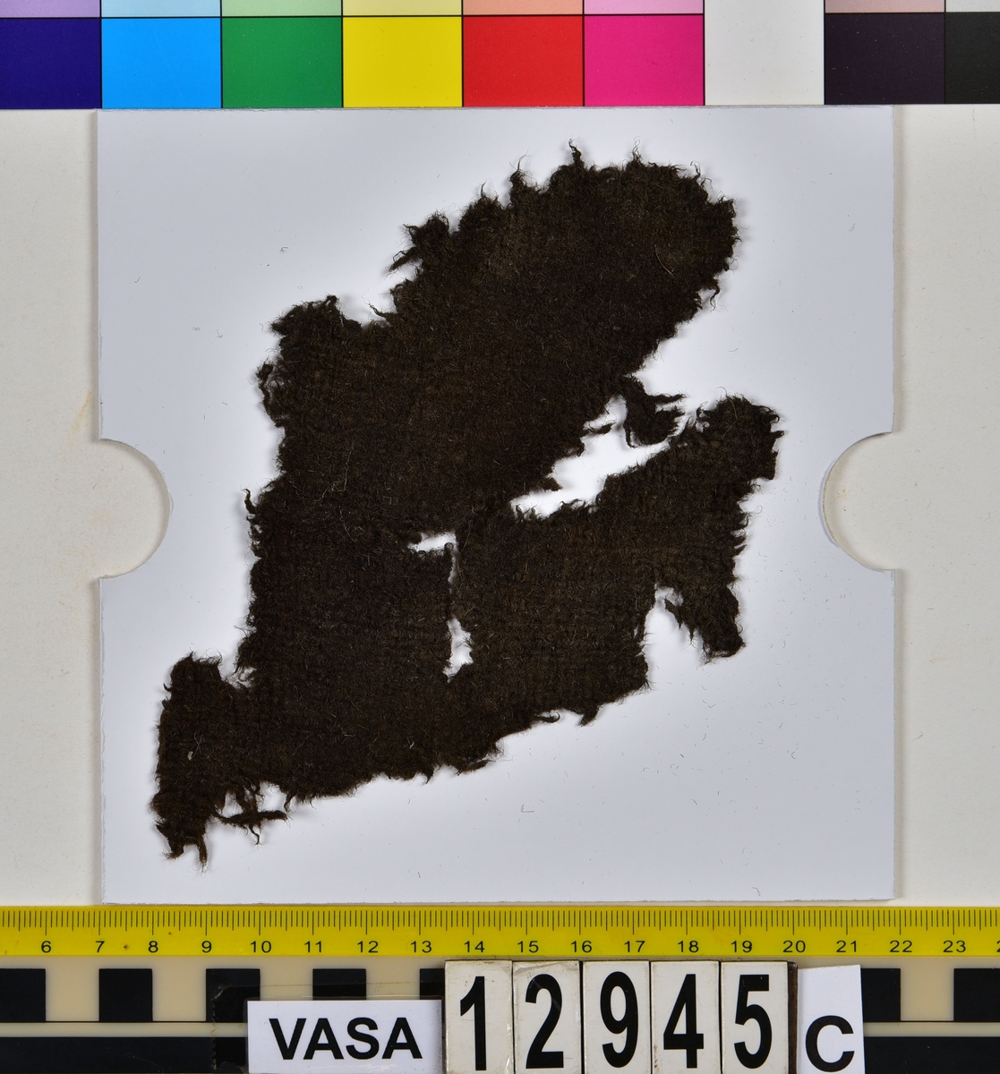 Textilfragment.
15 textilfragment uppdelade på fyndnummer 12945a-g.
Fnr 12945a består av fyra fragment av ull vävda i tuskaft. Två av fragmenten har rester av söm eller fåll samt har varit valkade.
Fnr 12945b består av två fragment av ull vävda i tuskaft. 
Fnr 12945c består av ett fragment av ull vävt i tuskaft. Fragmentet kan ha varit valkat på ena sidan.
Fnr 12945d består av ett fragment av ull vävt i tuskaft. Fragmentet har en söm med rester av stygn kvar i ena kanten.
Fnr 12945e består av tre fragment av ull vävda i tuskaft. Fragmentet har en tydlig originalkant bevarad.
Fnr 12945f består av ett filtat fragment. Kan möjligen ha varit en del av ett hattbrätte.
Fnr 12945g består av tre filtade fragment, troligen av ull.
