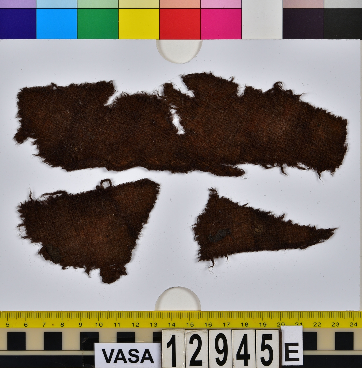 Textilfragment.
15 textilfragment uppdelade på fyndnummer 12945a-g.
Fnr 12945a består av fyra fragment av ull vävda i tuskaft. Två av fragmenten har rester av söm eller fåll samt har varit valkade.
Fnr 12945b består av två fragment av ull vävda i tuskaft. 
Fnr 12945c består av ett fragment av ull vävt i tuskaft. Fragmentet kan ha varit valkat på ena sidan.
Fnr 12945d består av ett fragment av ull vävt i tuskaft. Fragmentet har en söm med rester av stygn kvar i ena kanten.
Fnr 12945e består av tre fragment av ull vävda i tuskaft. Fragmentet har en tydlig originalkant bevarad.
Fnr 12945f består av ett filtat fragment. Kan möjligen ha varit en del av ett hattbrätte.
Fnr 12945g består av tre filtade fragment, troligen av ull.
